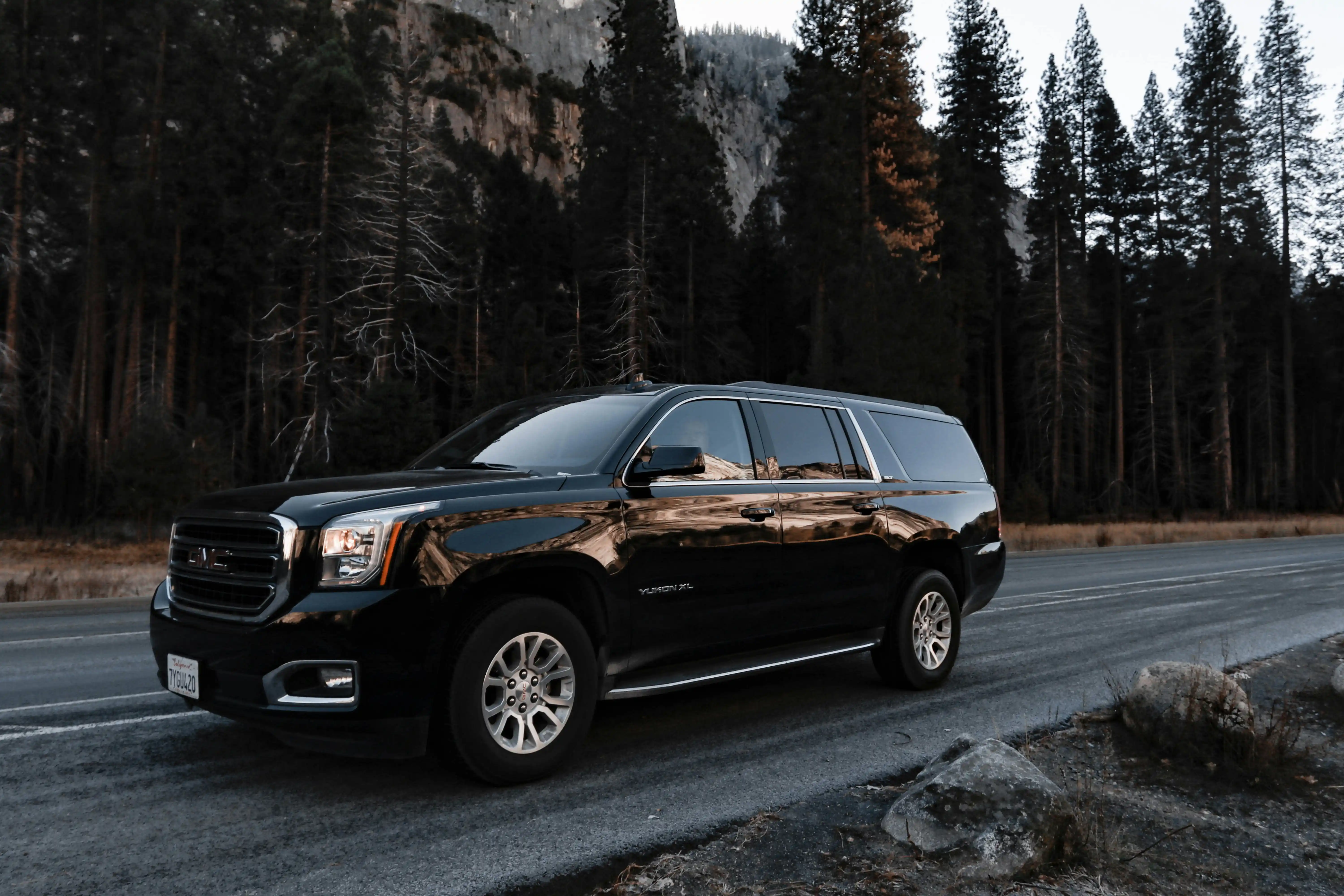 Black Cadillac Escalade waiting at the SeaTac Airport arrivals curb, professional chauffeur beside the rear passenger door, realistic Pacific Northwest setting